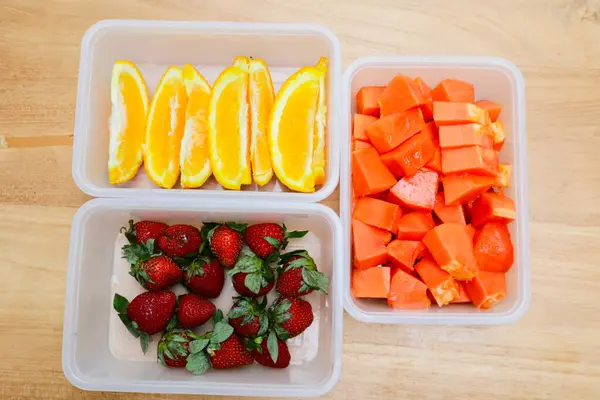 Tahta arka planda papaya, çilek ve portakal içeren plastik kaplar.