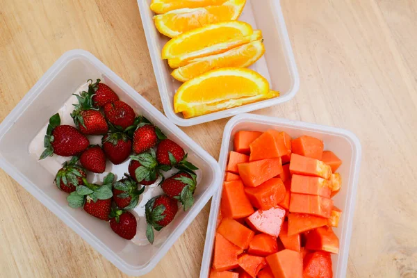 Tahta arka planda papaya, çilek ve portakal içeren plastik kaplar.