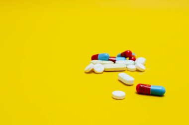 Sarı zemin üzerinde izole edilmiş ilaç kapsüllerinin ve tabletlerin fotoğrafı