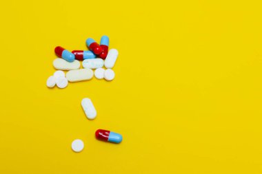 Sarı zemin üzerinde izole edilmiş ilaç kapsüllerinin ve tabletlerin fotoğrafı