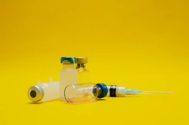 Sarı arka planda izole edilmiş şırınga ve ilaç şişelerinin fotoğrafları.