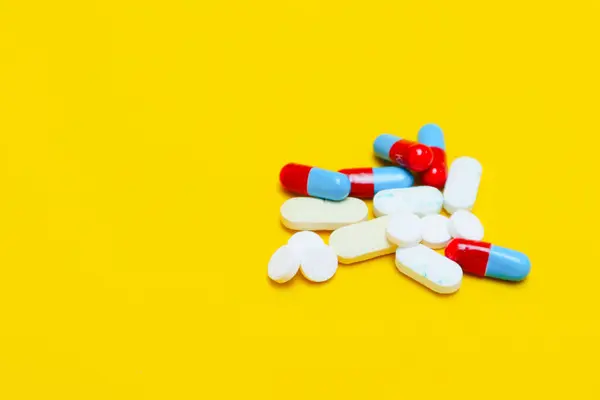 photo of medicine capsules and tablets isolated on yellow background