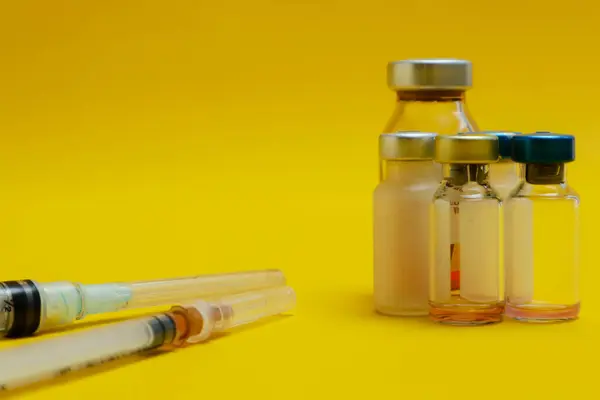 photo of several vials of injection medicine and syringes isolated on a yellow background