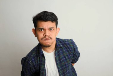 Asyalı genç bir adamın portresi somurtkan ve hayal kırıklığına uğramış bir yüz ifadesi, beyaz bir arka planda izole edilmiş.