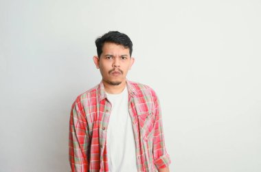 Asyalı genç bir adamın portresi somurtkan ve hayal kırıklığına uğramış bir yüz ifadesi, beyaz bir arka planda izole edilmiş.