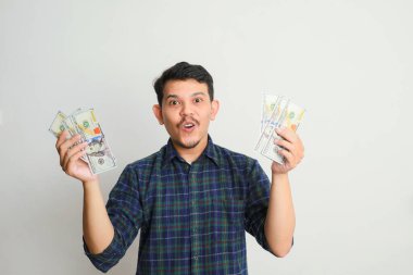 Asyalı genç bir adamın portresi, elinde bir dolar banknot tutarken mutlu bir ifade sergiliyor, beyaz bir arka planda izole edilmiş.