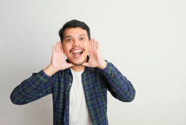 Genç, mutlu Asyalı bir adam, beyaz stüdyo arka planında izole edilmiş elleri bardağında bilgi veriyor.