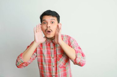 Genç, mutlu Asyalı bir adam, beyaz stüdyo arka planında izole edilmiş elleri bardağında bilgi veriyor.