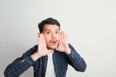 Genç, mutlu Asyalı bir adam, beyaz stüdyo arka planında izole edilmiş elleri bardağında bilgi veriyor.