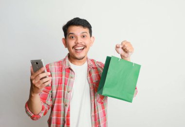 Alışveriş torbaları ve akıllı telefonu taşıyan gülümseyen yakışıklı Asyalı adamın portresi. Çevrimiçi dükkan konsepti.