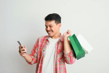 Alışveriş torbaları ve akıllı telefonu taşıyan gülümseyen yakışıklı Asyalı adamın portresi. Çevrimiçi dükkan konsepti.