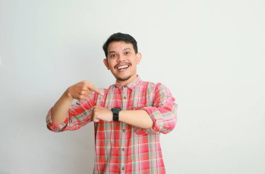 Heyecanlı Asyalı sıradan gömlekli bir adamın portresi kol saatine bakıyor, saati hatırlatıyor. Reklam konsepti. Beyaz arkaplanda izole edilmiş resim