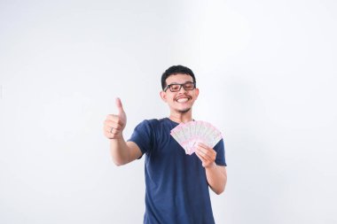 Heyecanlı genç yakışıklı Asyalı adam elinde bir deste para tutuyor beyaz arka planda izole edilmiş.