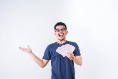 Heyecanlı genç yakışıklı Asyalı adam elinde bir deste para tutuyor beyaz arka planda izole edilmiş.