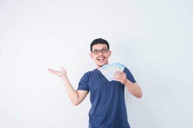 Heyecanlı genç yakışıklı Asyalı adam elinde bir deste para tutuyor beyaz arka planda izole edilmiş.
