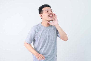 Genç, mutlu Asyalı bir adam, beyaz stüdyo arka planında izole edilmiş elleri ağız çevresine dolamış bir şekilde bilgi veriyor. reklam kavramları