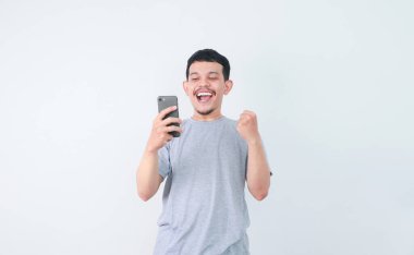 Bir adam yumruğunu sıktı ve elinde tuttuğu cep telefonuna baktığında şaşırmış bir yüz ifadesi sergiliyor.