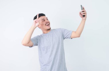 Yetişkin Asyalı adam mutlu bir ifadeyle selfie çekiyor.