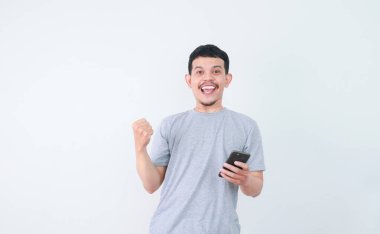 Bir adam yumruğunu sıktı ve elinde tuttuğu cep telefonuna baktığında şaşırmış bir yüz ifadesi sergiliyor.