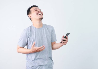 Gri tişörtlü neşeli bir genç elinde akıllı bir telefonla kahkaha atıyor.