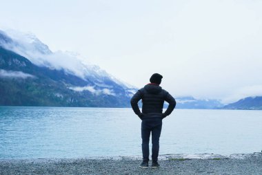 İsviçre 'de Brienz Gölü' nün kenarında duran Asyalı bir adam Alpler 'in manzarasına hayran.
