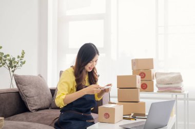 Genç bir kadın ambalaj sırasında cep telefonu ya da dijital kamerayla fotoğraf çekiyor. İnternete çevrimiçi satış yapmak ve ürün paketini hazırlamak için. İnternet üzerinden fikir satmak