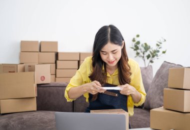 Genç bir kadın ambalaj sırasında cep telefonu ya da dijital kamerayla fotoğraf çekiyor. İnternete çevrimiçi satış yapmak ve ürün paketini hazırlamak için. İnternet üzerinden fikir satmak