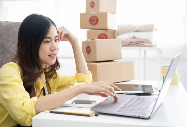 stock image Smiling happy asian woman checking orders from laptop, she owns an online store, she packs and ships through a private transport company. Online selling and online shopping concepts.