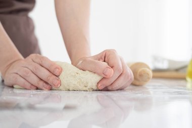 Masaya un serpiştirilmiş hamuru yoğuran bir kadın. Ev yapımı fırıncı şefi, makarna, pizza ve diğer hamur işlerini hazırlamak için un somunundan ekmek yapıyor..