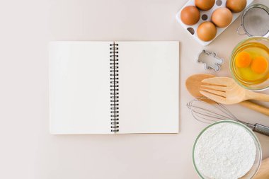Boş yemek tarifi kitabı, beyaz pişirme malzemeleri ve pembe arka planda mutfak malzemeleri. Kopyalama alanı olan üst görünüm.