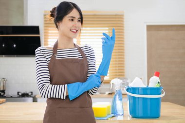 Mutfak masasında lastik eldivenli bir kadınla bir kova dolusu ev gereçleri..
