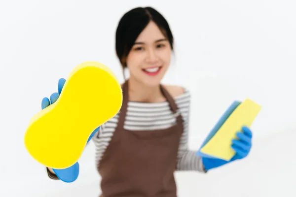 快乐的年轻女性 戴着蓝色橡胶手套进行护手 拿着海绵 对着相机微笑 同时在白色背景下清扫房子 — 图库照片
