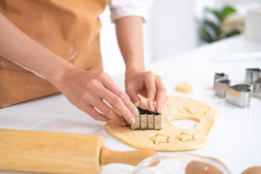 Ev yapımı bisküvi yapıyorum. Masanın üzerinde hamur ve diğer mutfak malzemeleriyle birlikte kurabiye kalıpları var. Ağaç, kalp ve yıldız şeklinde şirin bebek kurabiyeleri. Pişirme araçlarıyla pişirme.