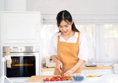 Çilek doğrayan meyveli tart yapan güzel bir kadın. Sağlıklı beslenme tarzı konsept portresi güzel bir genç kadının mutfakta çilekli ve yabanmersinli tart hazırlaması..