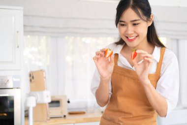 Sosyal medya etkileyicisi. Yemek blogcusu içerik yaratıyor. Çilek tutan kadın aşçı, kamerayla tripoda çekim yapıyor. Fırıncı çevrimiçi kursları, canlı yayın. Mutfakta yemek vlogcusu.