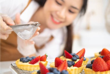 Genç ve güzel bir kadın mutfakta, fırında ve kahve dükkanında yemek pişiriyor. Çilekli taze meyveli taze pişmiş tart. Fırın ve kahve dükkanı işi..