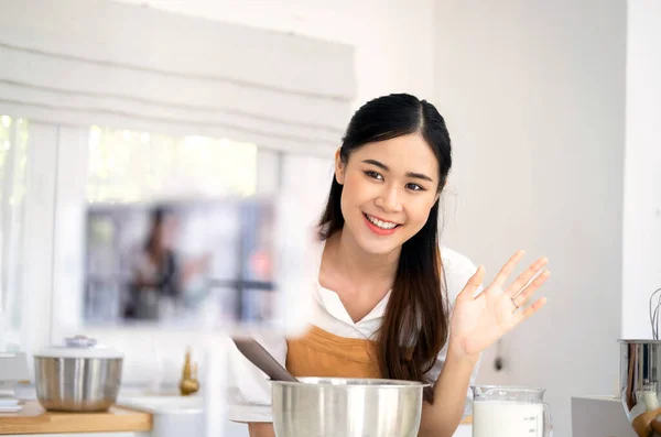 stock image baker online courses. food preparation and culinary training class concept. smiling woman chef prepare ingredients in the kitchen and shooting video of herself using mobile phone on a tripod.