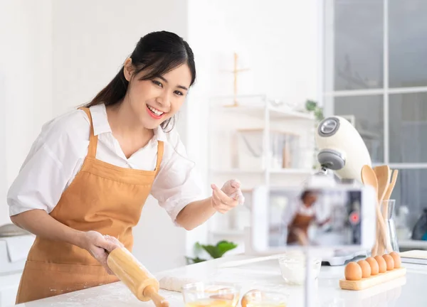 パン屋のオンラインコース 調理や料理の訓練の授業のコンセプトです キッチンでパン生地を練ったり三脚で携帯電話で自分のビデオを撮ったりするアジア料理人の笑顔 — ストック写真