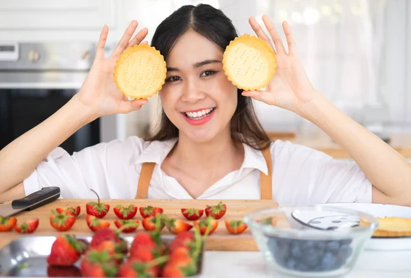 Attractive young woman is cooking in kitchen. Having fun while making strawberry blueberry fruit tart. Young woman holding tart in the kitchen. Home recipe. Cook at home. Stay at home.