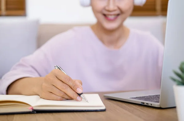 El kapama - öğrenci internetten Skype öğretmeniyle kablosuz kulaklık takıyor, mutlu genç kadın dil öğreniyor ders veriyor Webinar 'ı not yazarken izleyin evde dizüstü bilgisayara bakın, uzaktan eğitim alın