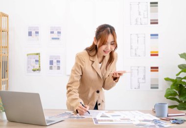 İç mimar müşteriyle cep telefonuyla konuşuyor, yeni projeyi tartışıyor, beyaz ofiste renk örnekleri ve malzemeler çiziyor, tasarım geliştiriyor, Boşluğu Kopyala