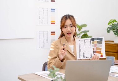 Asyalı iç mimar dizüstü bilgisayarın önünde oturmuş müşteriyle görüntülü konuşma yapıyor ve oturma planı ile pantone 'un mimarisini gösteriyor. iş ve modern teknoloji, toplantı ve çevrimiçi konferans.
