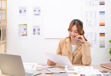 Genç Asyalı iç mimar ya da tasarımcı çizim, materyal örnek dizüstü bilgisayar ile birlikte yaratıcı bir proje üzerinde çalışıyor. Emlak işi, ev dekorasyonu ve yenileme konsepti.