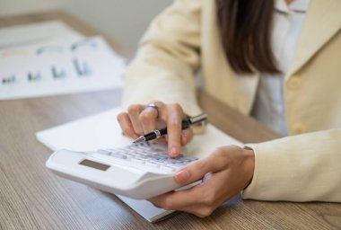 Close-up woman hand press calculator to calculate the company's financial results On the wooden table in the office and business work background, tax, accounting, statistics, and analytical research.