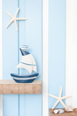 Yazın deniz dekorasyonu arka planında yelkenli, denizyıldızı ve deniz kabuğunun ön görüntüsü mavi beyaz duvarın üzerinde ahşap rafta. .