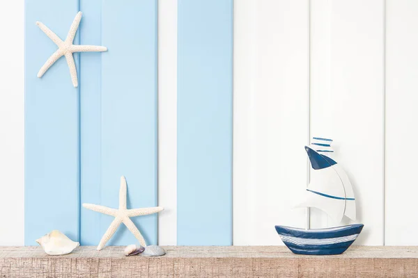Summer sea decoration background - Front view of sailboat , starfish and seashell on wooden shelf over blue white wall .