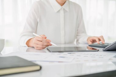 Çalışma yerinde hesap makinesi ve tablet kullanan modern iş kadını.