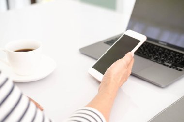 Asyalı iş kadını dizüstü bilgisayar kullanıyor ve akıllı telefonu kontrol ediyor, pencerenin önündeki temiz görüntüyü yumuşak ışıkta kapat.