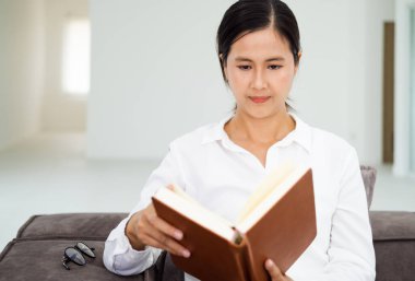 Modern oturma odasındaki kanepede kitap okuyan güzel, gülümseyen kadın. Evde iyi eğlenceler..