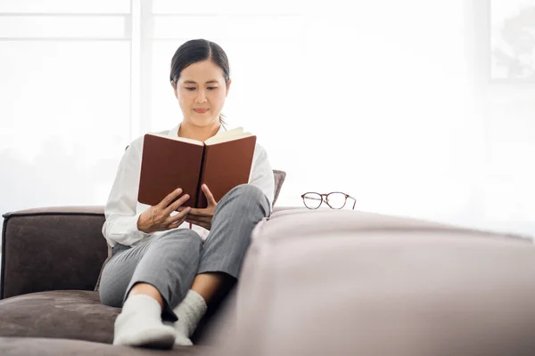 Gray cozy sofa couch and a beautiful asian woman, reading a book, concepts of home and comfort, place for text copy space.